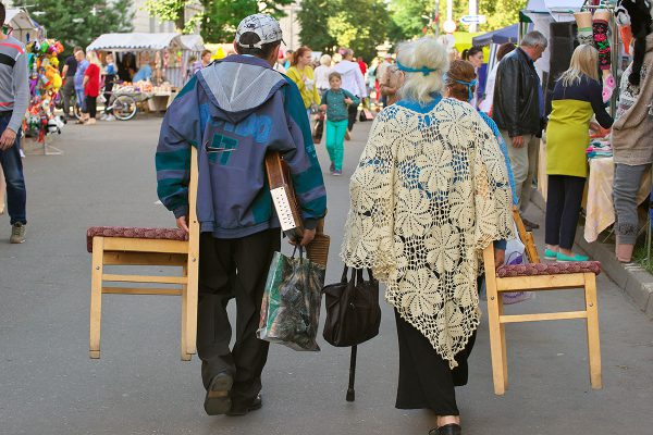 Пожилая пара несет стулья и музыкальные инструменты после выступления в Городе мастеров на «Славянском базаре в Витебске». Фото Сергея Серебро